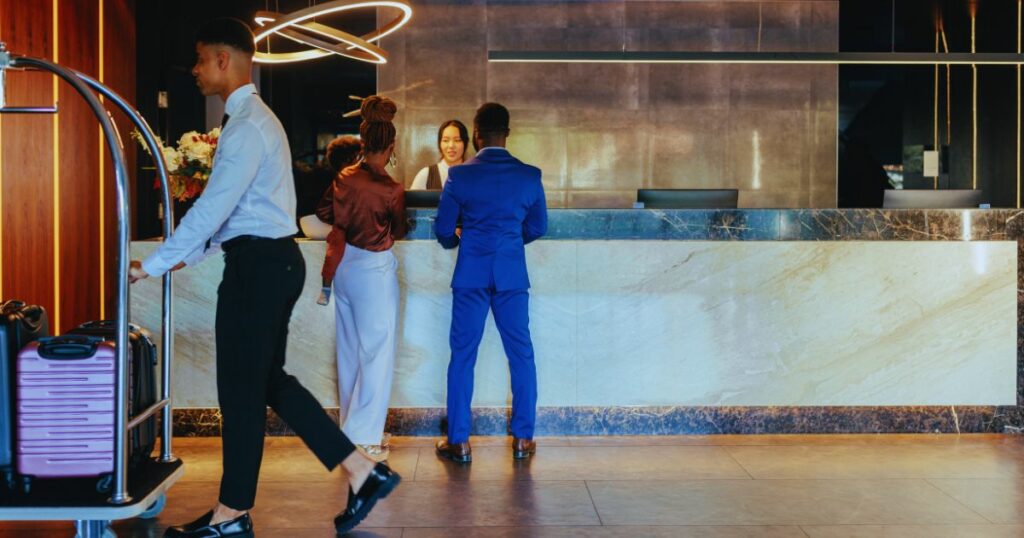Image of a hotel lobby with a couple checking into their room and a person walking past with a suitcase